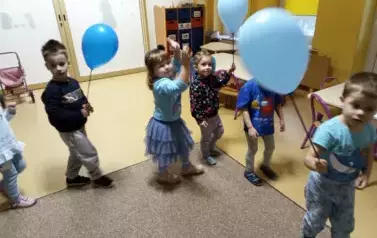 dzieci idą po kole z niebieskimi balonami