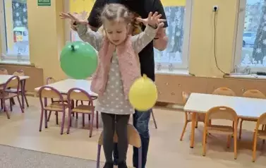 dziecko stoi na krześle z balonami