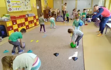 dzieci turlają piłki między pachołkami