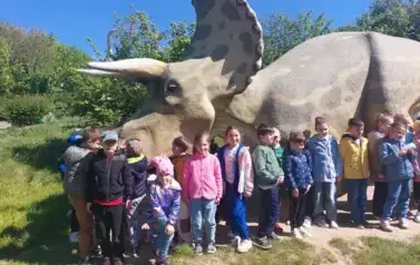 dzieci pozują do zdjęcia przy dinozaurze