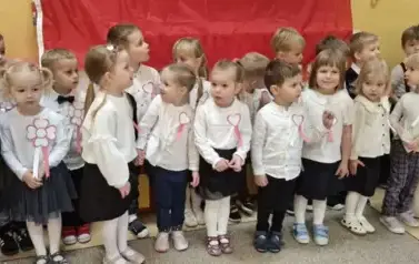 dzieci stoją na tle flagi Polski w galowych strojach