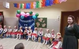 dzieci z grupy 2 siedzą na krzesełkach, nauczycielka wita rodzic&oacute;w