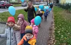 dzieci idą wok&oacute;ł przedszkola z niebieskimi balonami