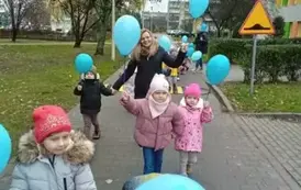 dzieci idą wok&oacute;ł przedszkola z niebieskimi balonami