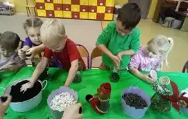 dzieci wsypują ziemię do słoik&oacute;w
