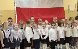 dzieci w galowych strojach na tle flagi Polski