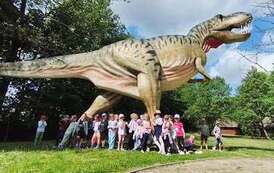 dzieci pozują do zdjęcia grupowego pod figurą dinozaura
