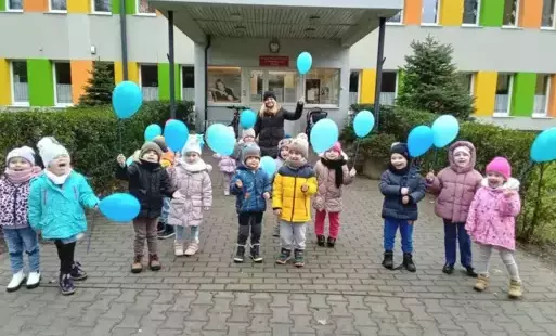 Dzieci przed przedszkolem z niebieskimi balonami
