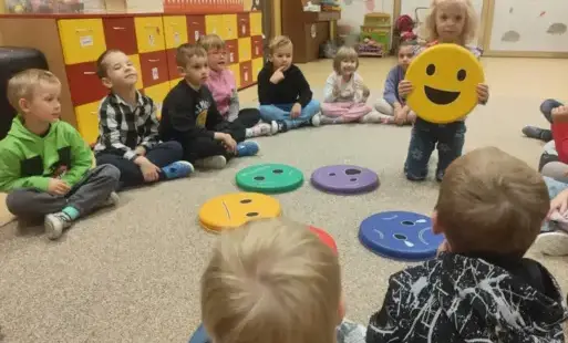 dzieci siedzą w kole, dziewczynka pokazuje symbol emocji