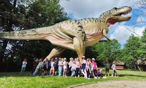 dzieci pozują do zdjęcia grupowego pod figurą dinozaura